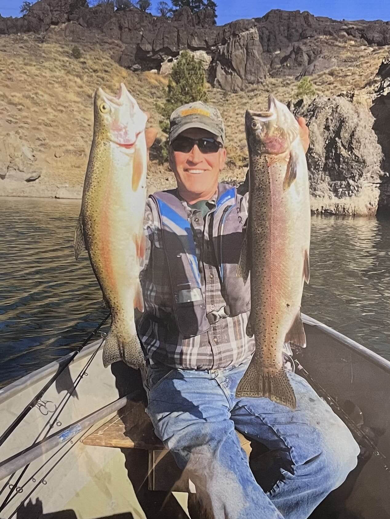 Man holding two large fish while sitting in a boat on a river.