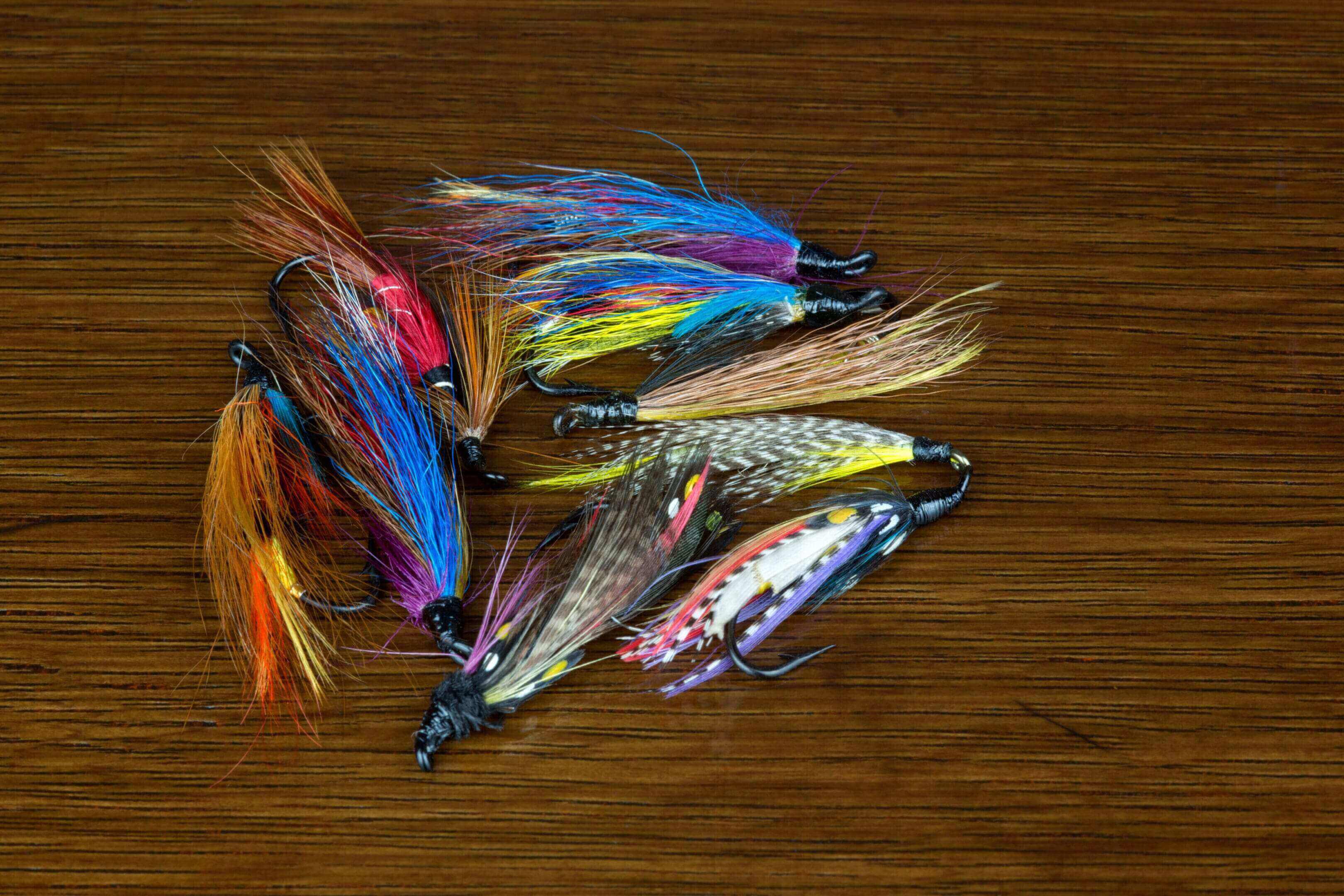 Colorful fishing flies arranged on a wooden surface.