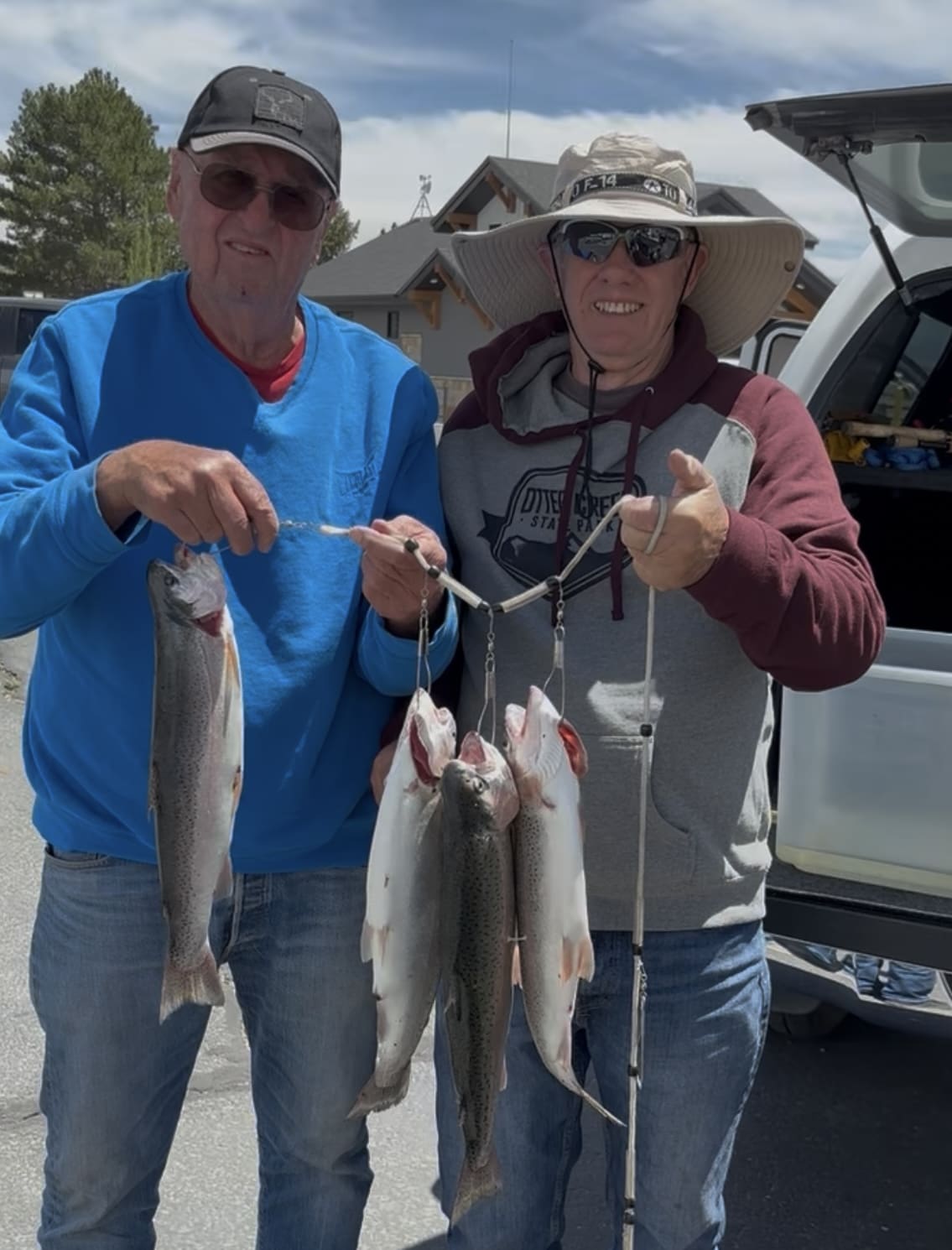 Two men proudly holding freshly caught fish near a vehicle.